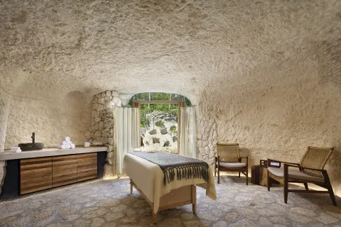 Single spa treatment room with stone walls and lounge chairs at Hotel Xcaret Arte.
