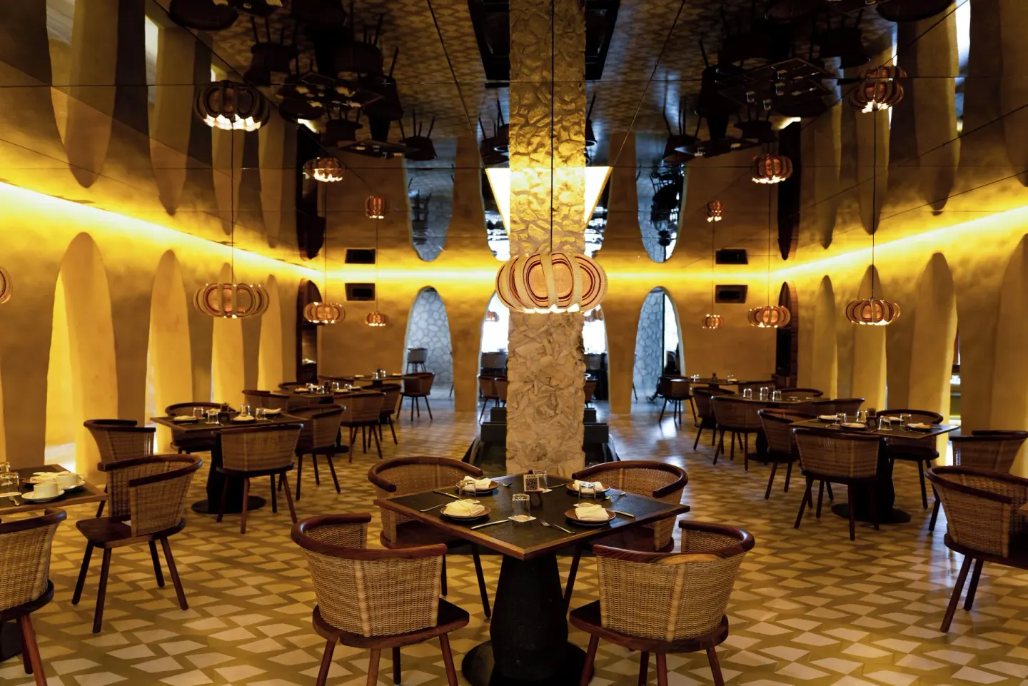 Warmly lit dining room with arched walls and woven chairs at Hotel Xcaret Arte.