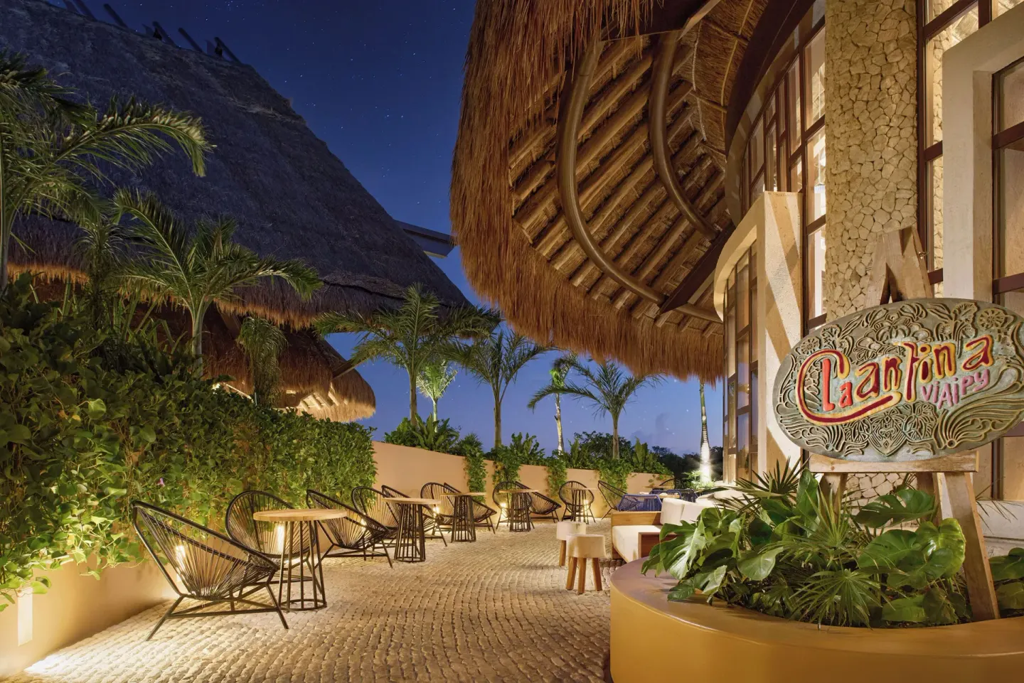 Cantina terrace with palapa roofs and a sign at Hotel Xcaret Arte.
