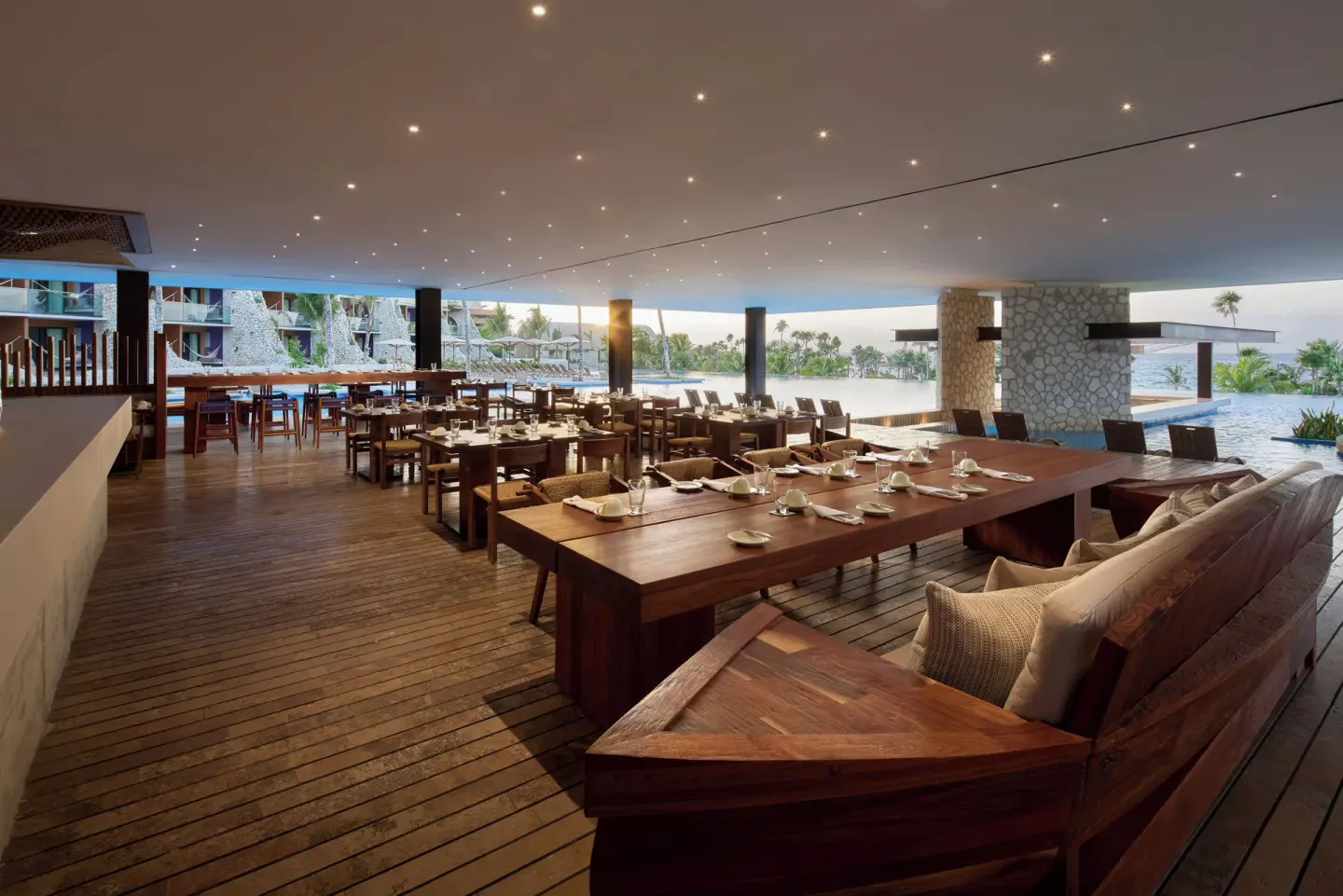 Open-air waterfront restaurant with wooden tables at Hotel Xcaret Arte.