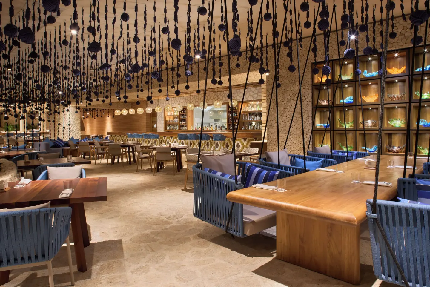 Restaurant dining room with hanging rope décor and blue swing chairs at Hotel Xcaret Arte.