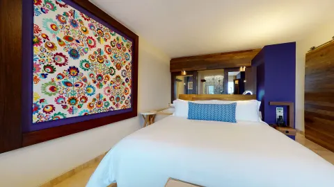 Junior Suite Ocean View king bed with colorful wall art at Hotel Xcaret Arte.