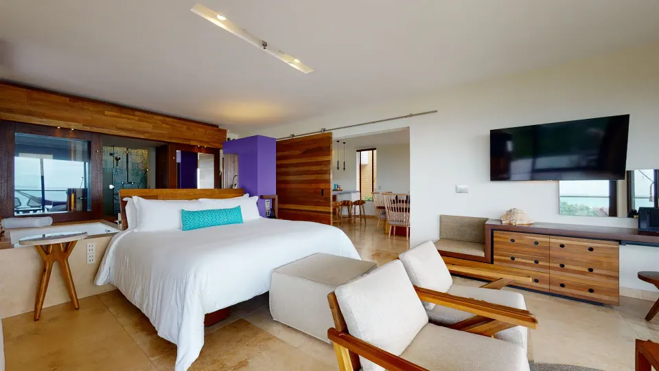 Junior Suite Oceanfront king bed and seating area at Hotel Xcaret Arte with a wall-mounted TV.