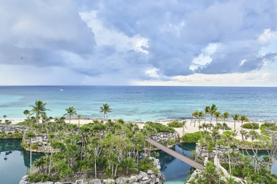 Oceanfront view from a Junior Suite at Hotel Xcaret Arte with beach, palms, lagoons and cloudy sky.