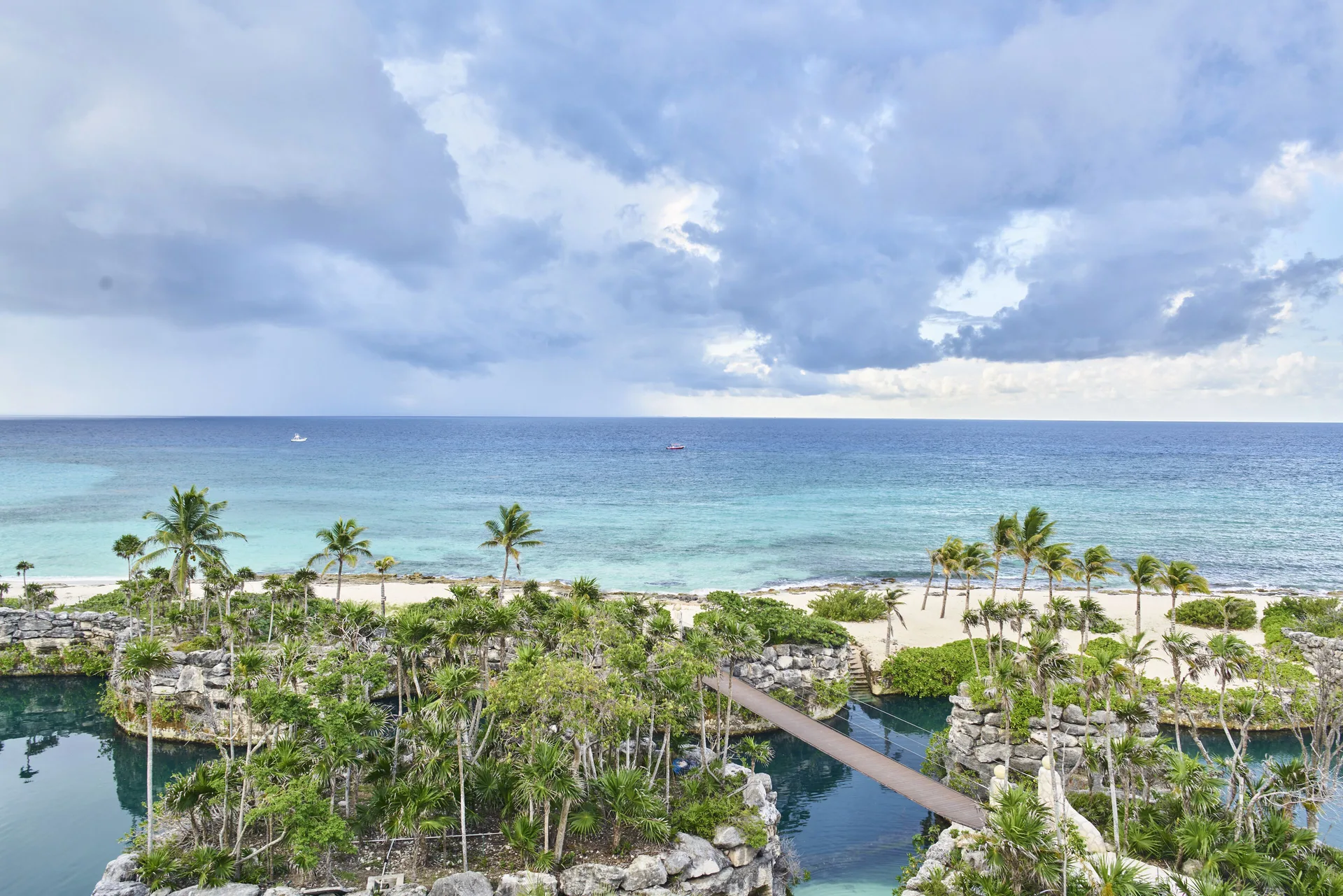 Oceanfront view from a Junior Suite at Hotel Xcaret Arte with beach, palms, lagoons and cloudy sky.