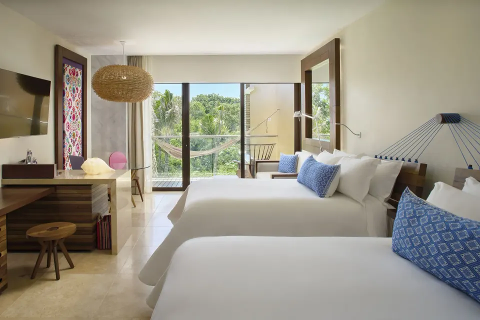 Garden suite with two beds, desk, hammock balcony, and greenery at Hotel Xcaret Arte.