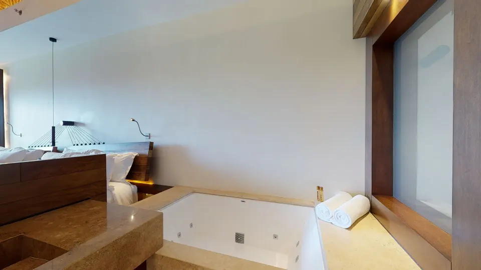 Suite garden bathtub beside the bed and window at Hotel Xcaret Arte.