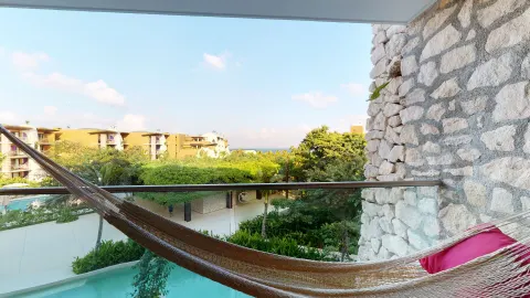 Suite Ocean View balcony hammock with greenery and distant ocean at Hotel Xcaret Arte.