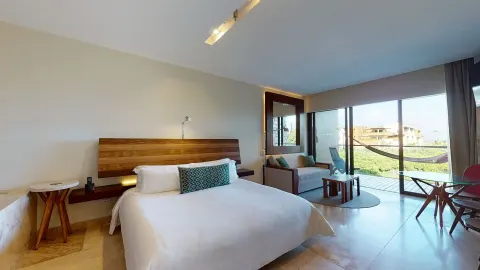 Suite Ocean View king bed beside lounge seating and balcony doors at Hotel Xcaret Arte.