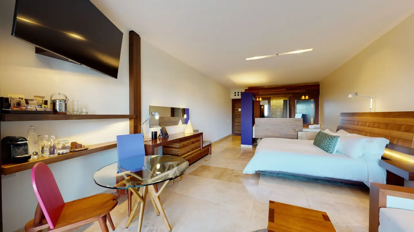 Suite Ocean View room with king bed, dining table, TV, and minibar shelves at Hotel Xcaret Arte.