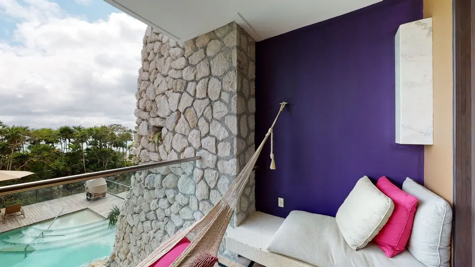 Oceanfront suite balcony at Hotel Xcaret Arte with hammock, daybed and pool view.