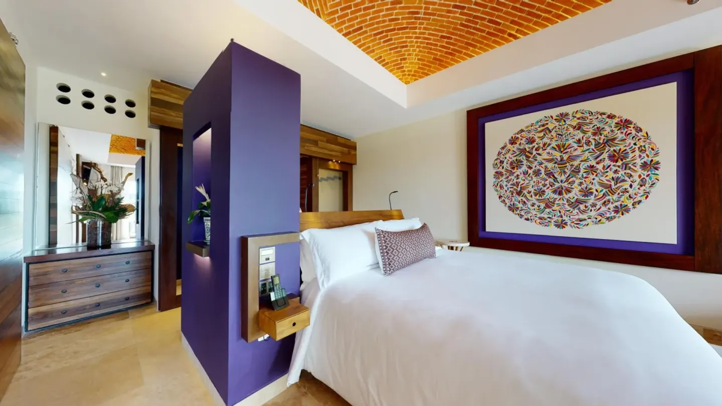 River View suite bed with colorful wall art and wood dresser at Hotel Xcaret Arte.