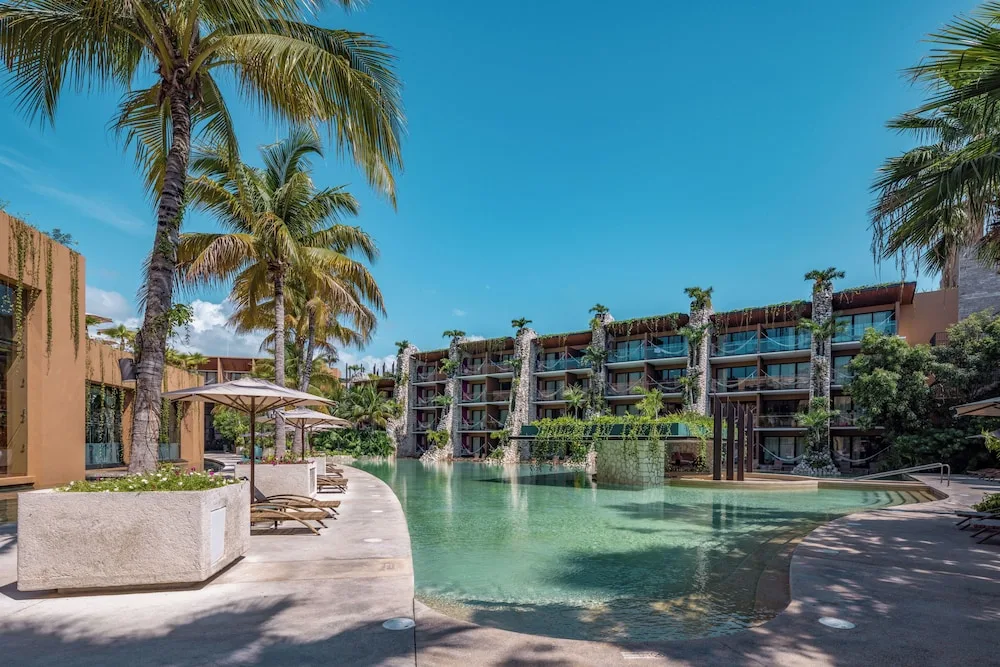 Curving resort pool with loungers, palms, and guest room balconies at Hotel Xcaret Mexico.