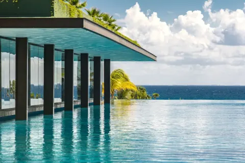 Infinity pool beside a glass-walled building overlooking the ocean at Hotel Xcaret Mexico.