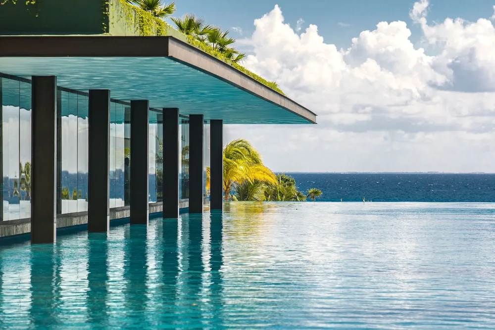 Infinity pool beside a glass-walled building overlooking the ocean at Hotel Xcaret Mexico.
