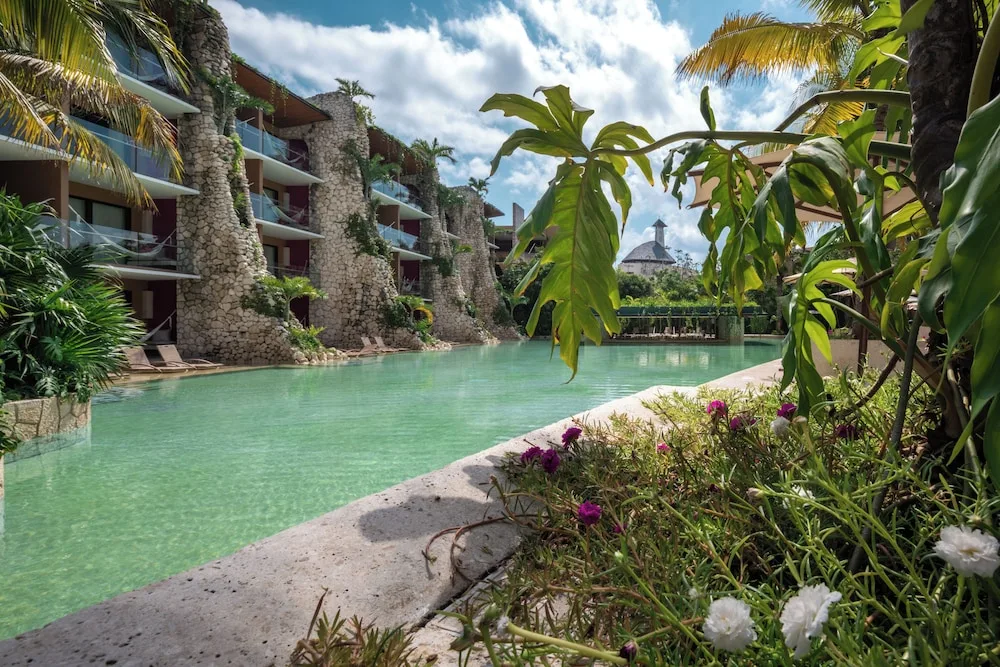 Lagoon-style pool beside guest room balconies and tropical plants at Hotel Xcaret Mexico.