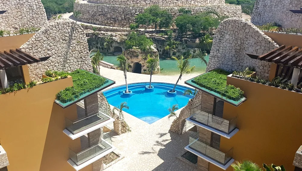 Resort pool framed by stone buildings and palms at Hotel Xcaret Mexico.