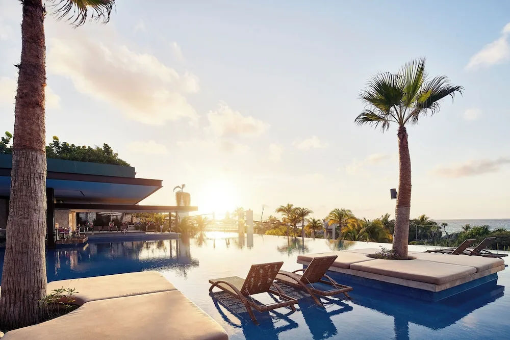Sunset infinity pool with loungers, palms, and ocean beyond at Hotel Xcaret Mexico.