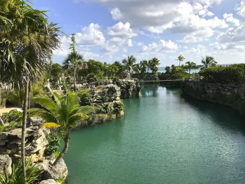 A turquoise lagoon winds through rock and palms at Hotel Xcaret Mexico.