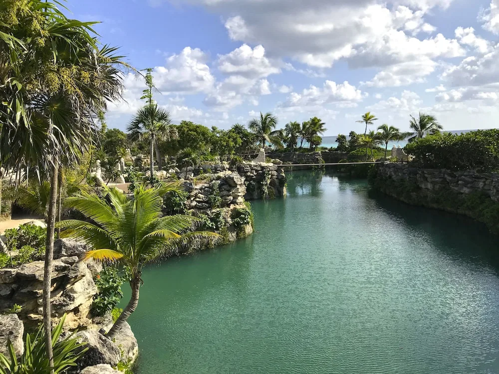 A turquoise lagoon winds through rock and palms at Hotel Xcaret Mexico.