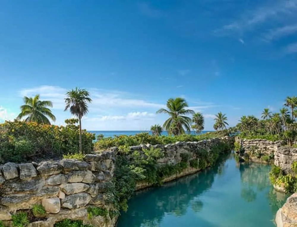 Rock-lined turquoise waterway with palms and ocean beyond at Hotel Xcaret Mexico.