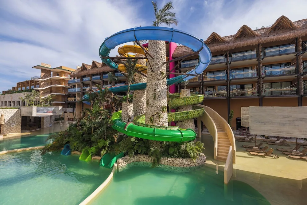 Colorful water slides winding over a pool beside rooms at Hotel Xcaret Mexico.