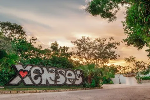Large Xcaret sign surrounded by tropical plants at sunset at Hotel Xcaret Mexico.