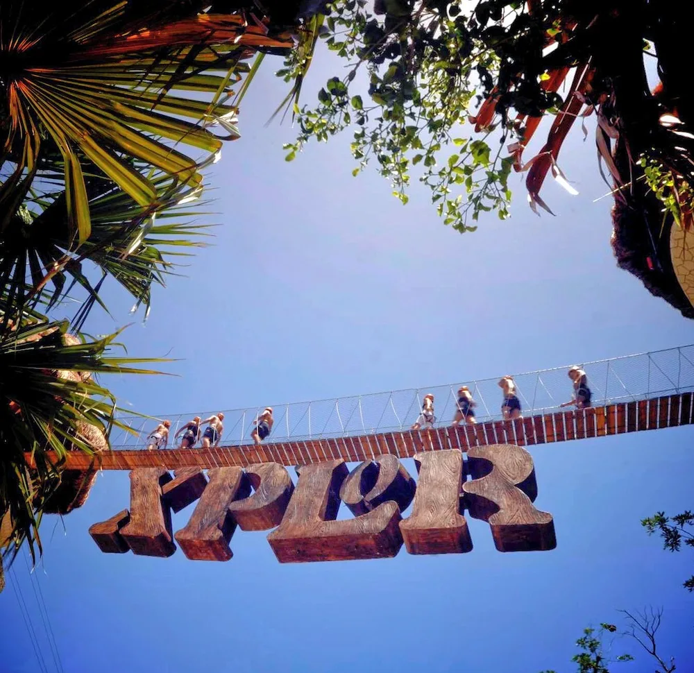 Suspension bridge with Xplor sign and visitors overhead at Hotel Xcaret Mexico.