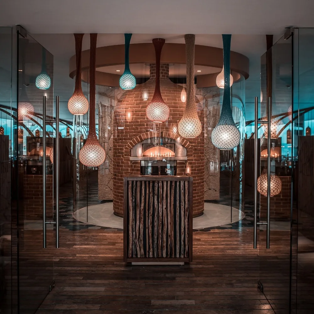 Restaurant entry with woven pendant lights and a brick oven at Hotel Xcaret Mexico.