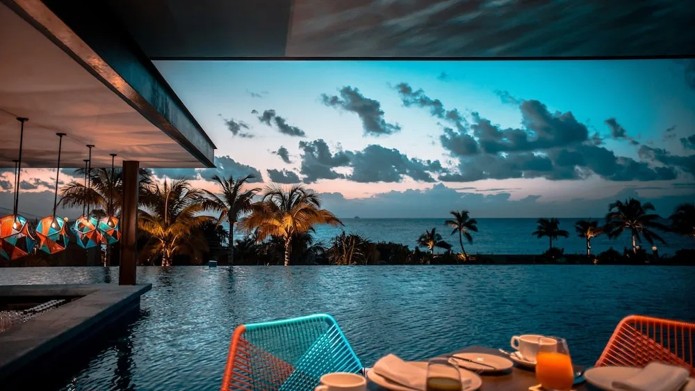 Poolside dining table facing an infinity pool and ocean at sunset at Hotel Xcaret Mexico.