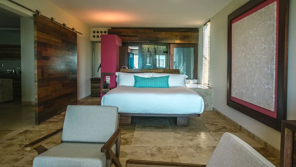 Junior Suite king bed with lounge seating and wood accents at Hotel Xcaret Mexico.