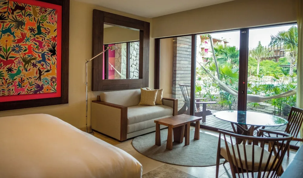 Suite Garden room seating area with bed edge and garden-facing balcony at Hotel Xcaret Mexico.