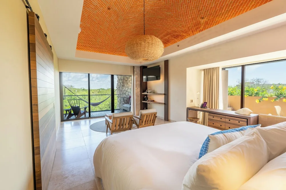 Master Suite king bed with balcony and hammock view at Hotel Xcaret Mexico.