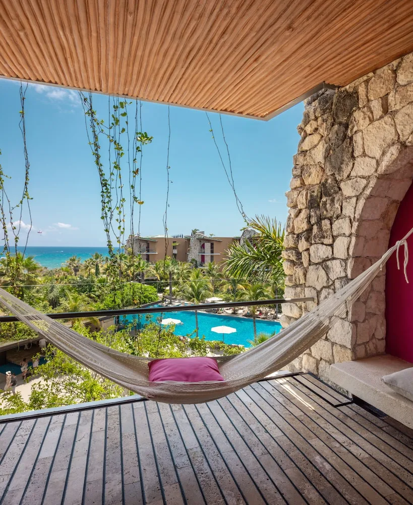 Suite Ocean View balcony at Hotel Xcaret Mexico with hammock, pool, palms, and ocean beyond.