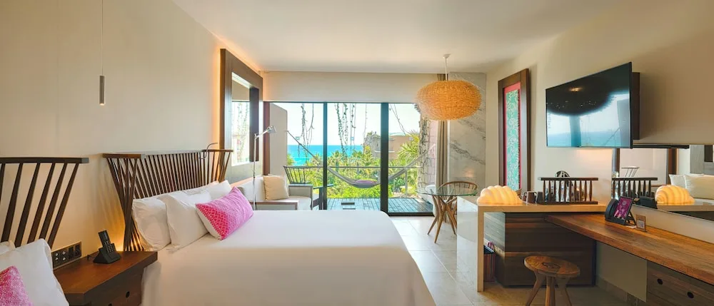 Suite Ocean View bedroom at Hotel Xcaret Mexico with two beds, desk, balcony, hammock, and ocean beyond.