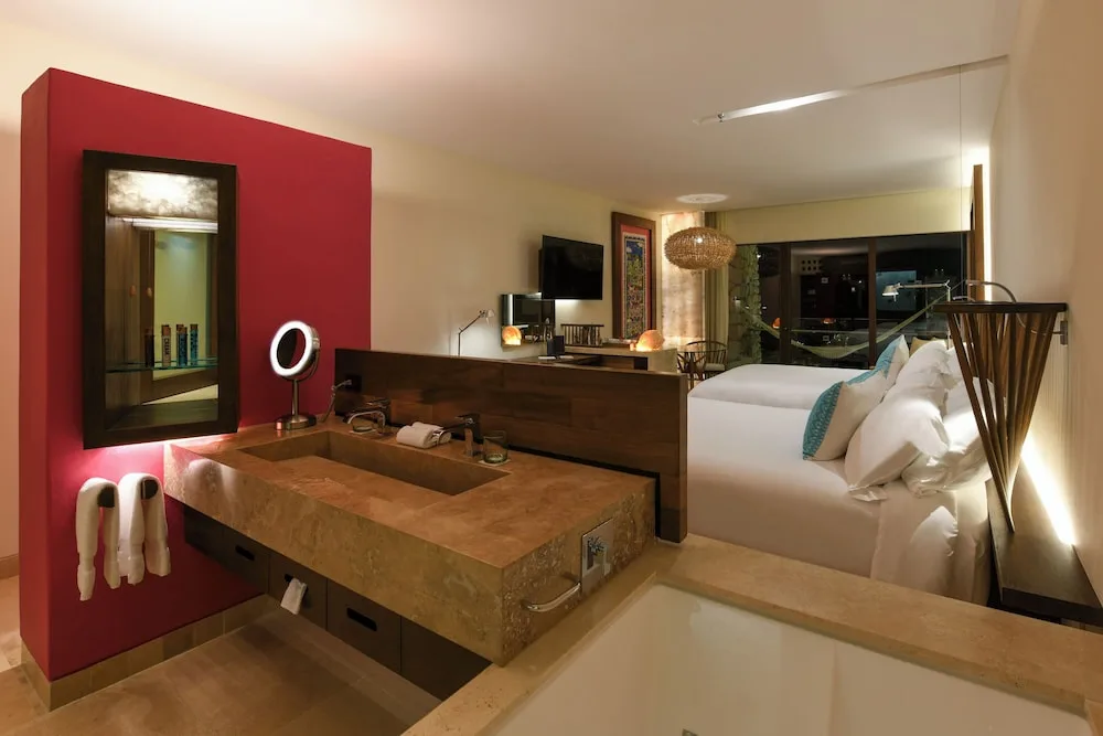 Suite Ocean View bathroom and two beds at Hotel Xcaret Mexico with vanity, tub, and balcony beyond.