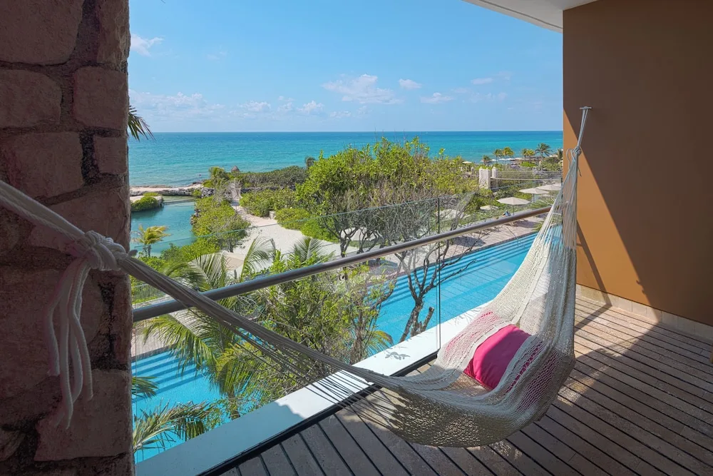 Oceanfront suite balcony with hammock overlooking pool, gardens, and sea at Hotel Xcaret Mexico.