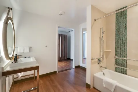 Accessible bathroom with tub, vanity and round mirror at Hyatt Centric Waikiki Beach.