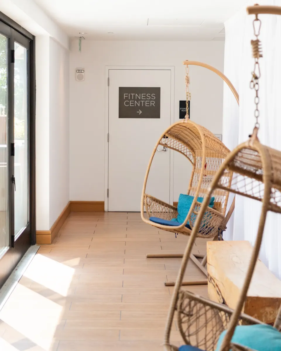 Indoor corridor at Hyatt Centric Waikiki Beach with wicker hanging chairs near a fitness center door.