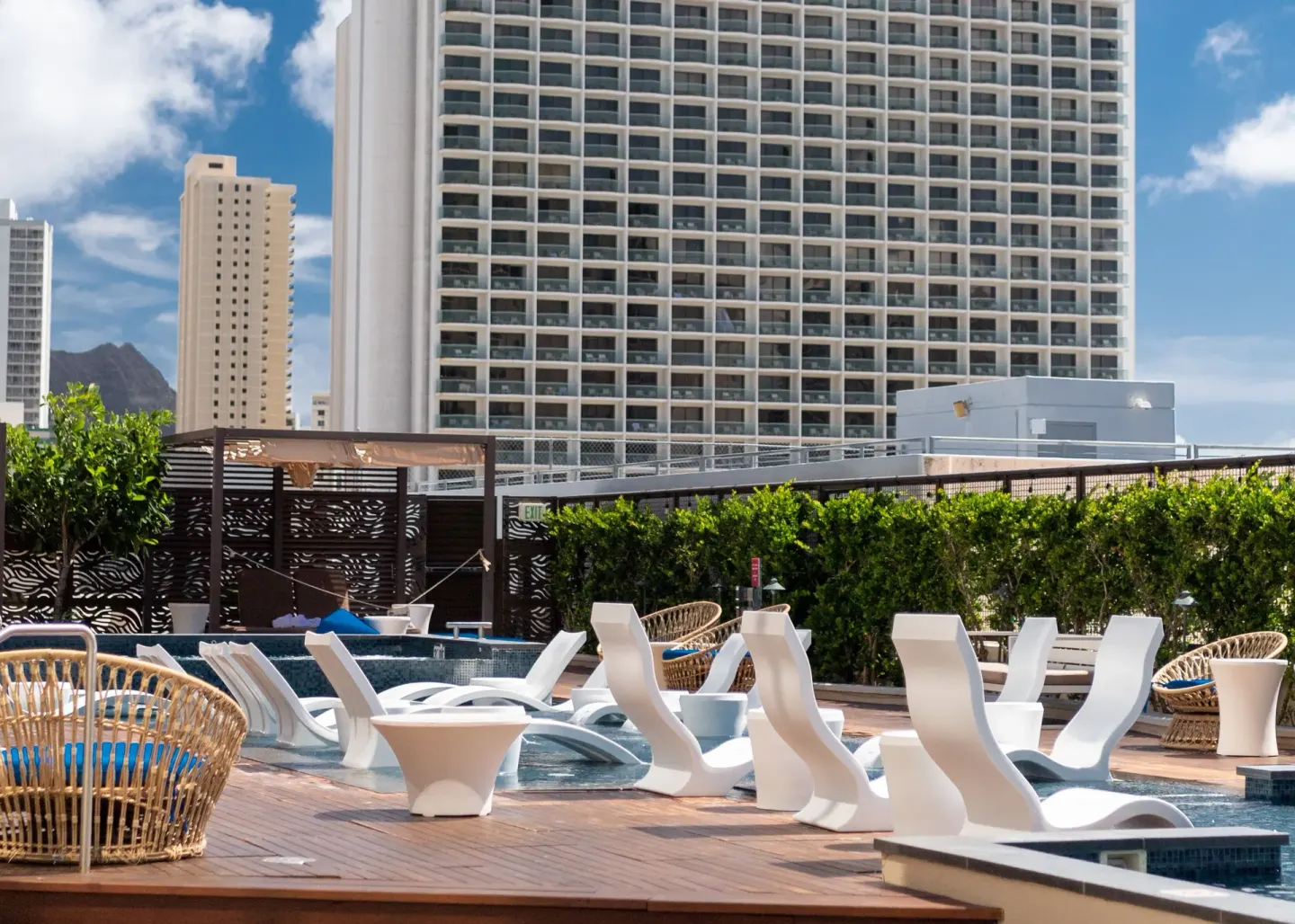 Daytime pool deck with in-water loungers and city buildings at Hyatt Centric Waikiki Beach.