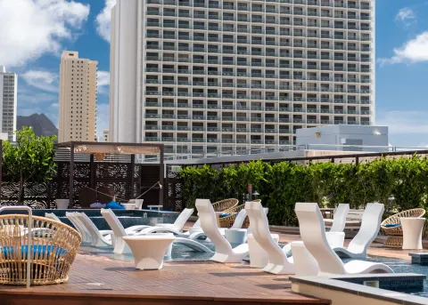 Daytime pool deck with in-water loungers and city buildings at Hyatt Centric Waikiki Beach.