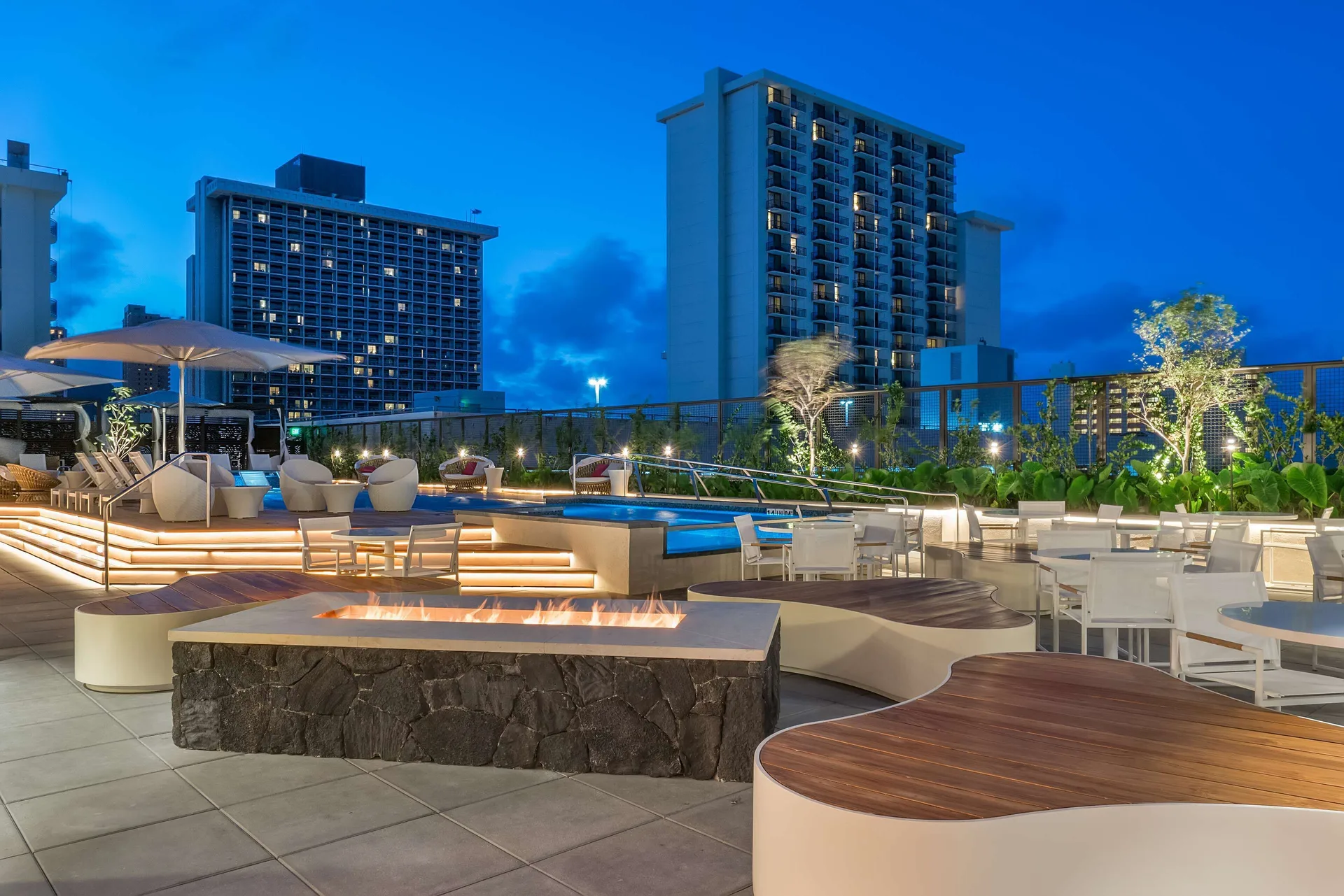 Evening pool terrace with fire feature and city buildings at Hyatt Centric Waikiki Beach.