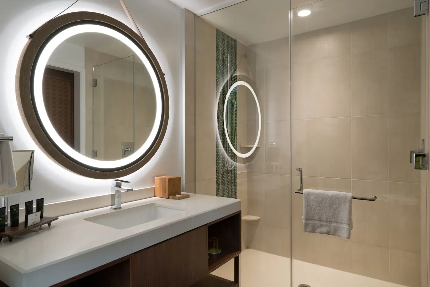 Guest bathroom with round lighted mirror and glass shower at Hyatt Centric Waikiki Beach.