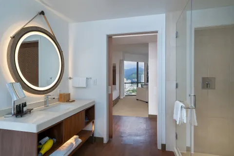 Guest bathroom with vanity, glass shower and bedroom view at Hyatt Centric Waikiki Beach.