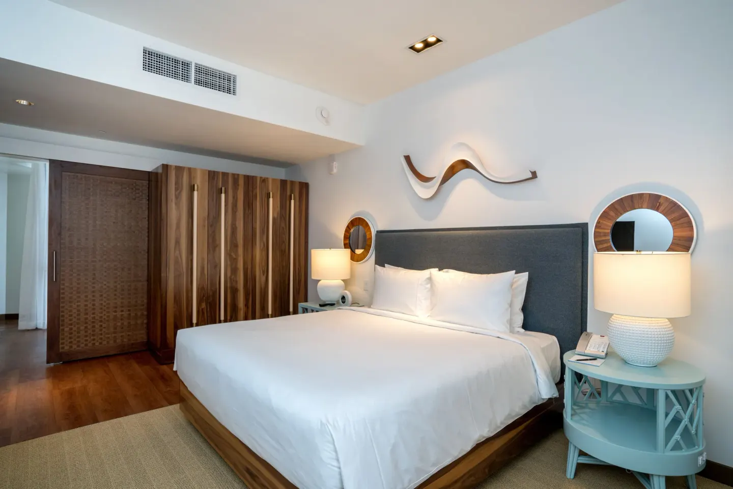 King-bed guest room with wood wardrobe and blue nightstands at Hyatt Centric Waikiki Beach.