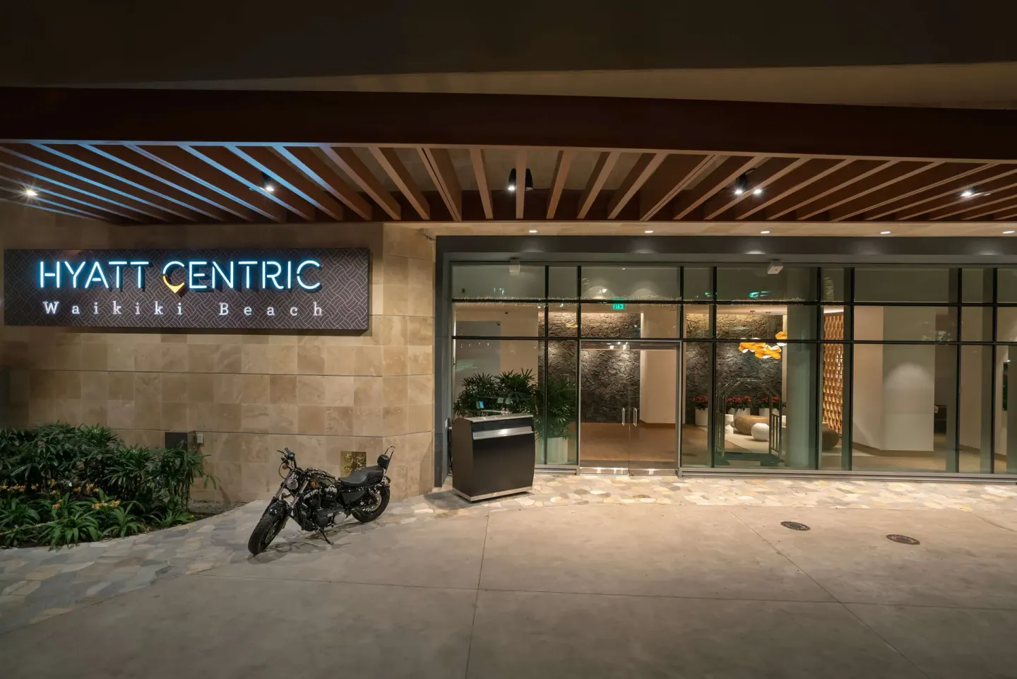 Illuminated entrance and glass doors at Hyatt Centric Waikiki Beach.