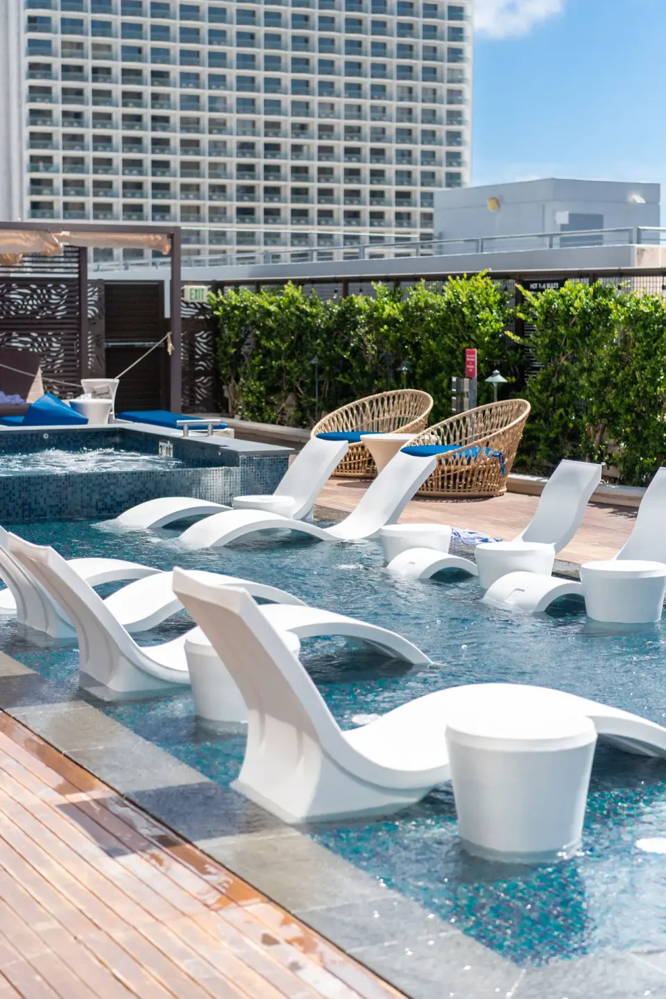In-water chaise loungers and wicker chairs at the pool at Hyatt Centric Waikiki Beach.