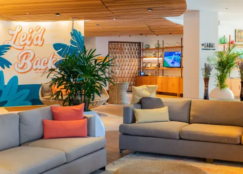 Lobby lounge at Hyatt Centric Waikiki Beach with sofas, plants, mural, and wood ceiling details.