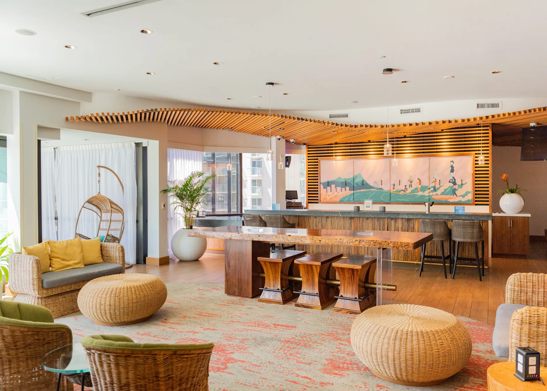 Open lobby lounge at Hyatt Centric Waikiki Beach with wicker seating, communal table, and bar counter.