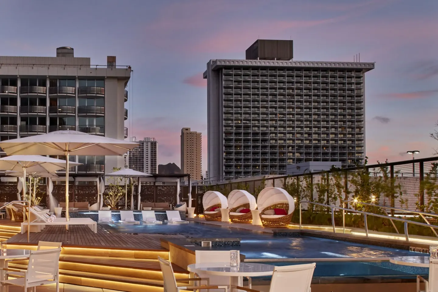 Pool deck with loungers and cabanas at Hyatt Centric Waikiki Beach at dusk.